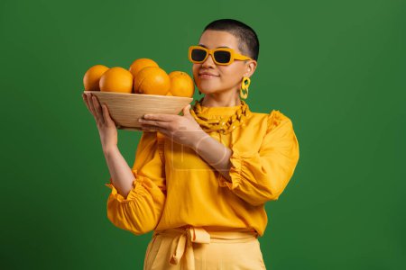 Photo for Beautiful young short hair woman carrying plate with oranges against green background - Royalty Free Image