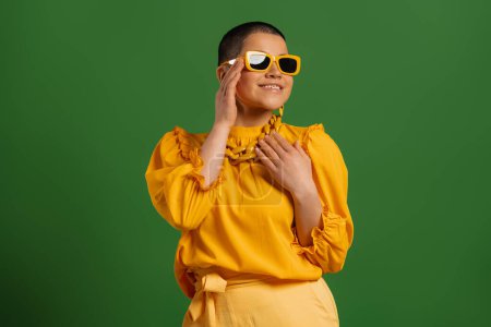 Téléchargez les photos : Jeune femme à la mode aux cheveux courts dans des lunettes à la mode souriant sur fond vert - en image libre de droit