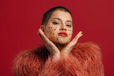 Photo for Fashionable short hair woman with shiny crystals over her face gesturing against red background - Royalty Free Image