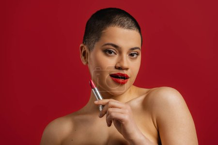 Photo for Beautiful young short hair woman holding lipstick against red background - Royalty Free Image