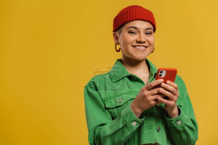 Foto de Mujer joven de moda usando el teléfono inteligente y sonriendo contra el fondo amarillo - Imagen libre de derechos