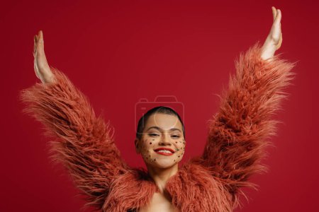 Foto de Juguetón joven mujer de pelo corto con cristales brillantes sobre su cara gestos contra el fondo rojo - Imagen libre de derechos