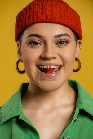 Téléchargez les photos : Portrait de belle jeune femme au chapeau tenant des lettres en plastique dans la bouche sur fond jaune - en image libre de droit