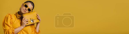 Téléchargez les photos : Jeune femme aux cheveux courts à la mode penchant la tête sur son sac à la mode sur fond jaune - en image libre de droit