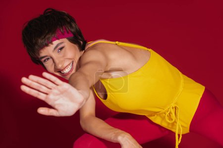 Photo for Happy young fit woman in retro styled sportswear stretching out hand against red background - Royalty Free Image