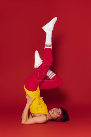Téléchargez les photos : Heureuse jeune femme en forme dans un style rétro vêtements de sport exercice sur fond rouge - en image libre de droit