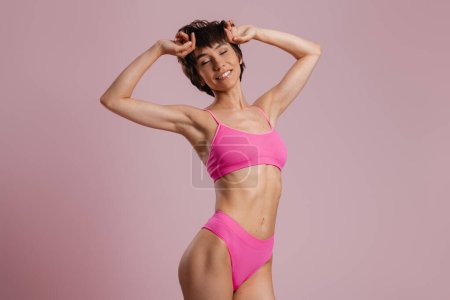 Photo for Beautiful young fit woman in underwear looking happy while standing against colored background - Royalty Free Image