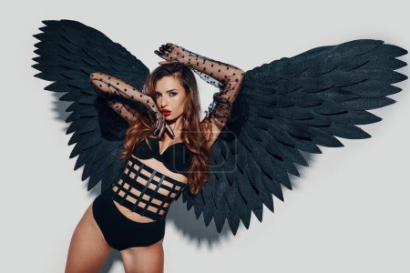 Téléchargez les photos : Jolie jeune femme en lingerie portant des ailes d'ange noir sur fond gris - en image libre de droit