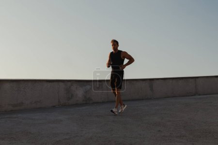 Téléchargez les photos : Jeune homme sportif en vêtements de sport courant sur la route tout en profitant du jogging matinal en plein air - en image libre de droit