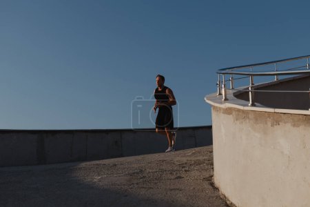 Téléchargez les photos : Jeune homme confiant dans les vêtements de sport en cours d'exécution par la route tout en appréciant le jogging matinal - en image libre de droit