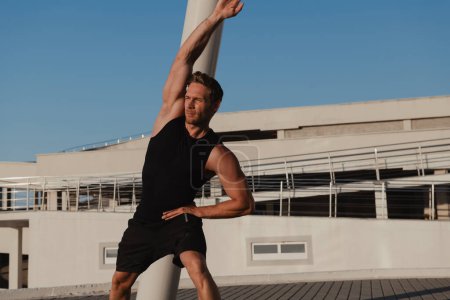 Téléchargez les photos : Confiant jeune homme musclé en vêtements de sport faisant des exercices matinaux à l'extérieur - en image libre de droit