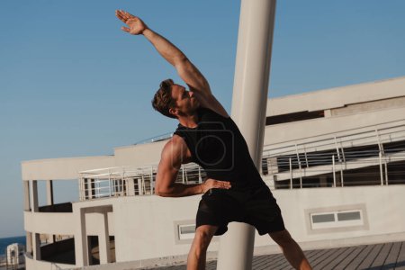 Téléchargez les photos : Beau jeune homme musclé en vêtements de sport faisant des exercices matinaux à l'extérieur - en image libre de droit