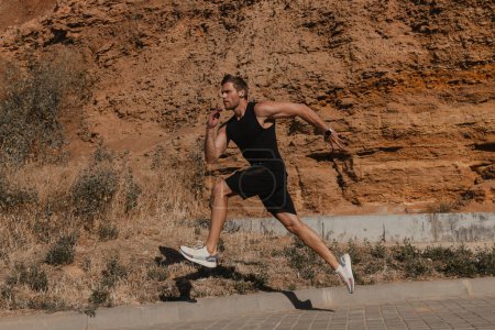Téléchargez les photos : Jeune homme sportif en vêtements de sport courant contre la montagne rocheuse à l'extérieur - en image libre de droit