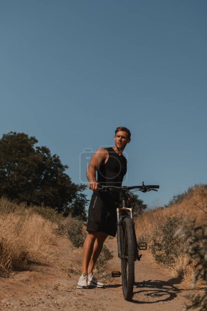 Téléchargez les photos : Jeune homme confiant en vêtements de sport debout près de son vélo de montagne à l'extérieur - en image libre de droit