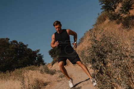 Téléchargez les photos : Homme athlétique confiant en vêtements de sport descendant la colline à l'extérieur - en image libre de droit