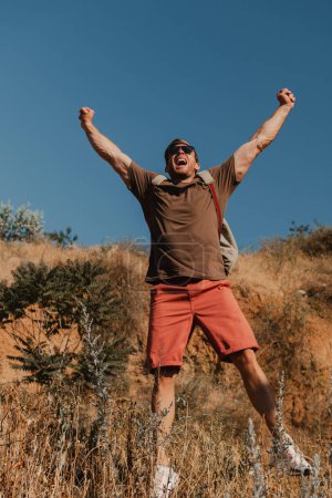 Photo for Joyful male adventurer with backpack gesturing while hiking in mountains - Royalty Free Image