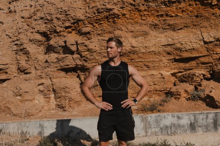 Photo for Muscular young man in sports clothing standing against rocky mountain outdoors - Royalty Free Image