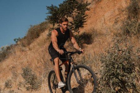 Téléchargez les photos : Jeune homme confiant en vêtements de sport équitation vélo par sentier de montagne à l'extérieur - en image libre de droit