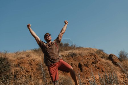 Téléchargez les photos : Heureux aventurier masculin avec des gestes de sac à dos lors de randonnées en montagne - en image libre de droit