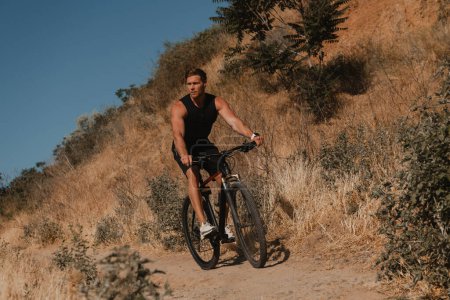 Photo for Confident young man in sports clothing riding bicycle by mountain hill outdoors - Royalty Free Image