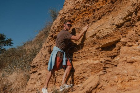 Photo for Confident male adventurer holding on grip while climbing the rock as extreme challenge - Royalty Free Image