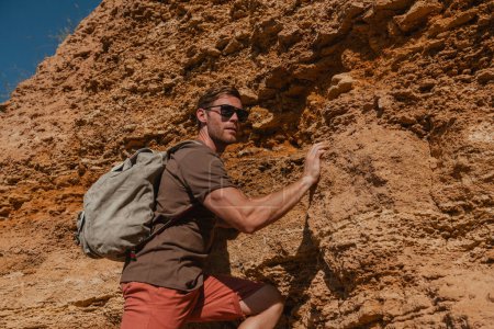 Téléchargez les photos : Jeune homme confiant tenant sur l'adhérence tout en escaladant le rocher comme défi extrême - en image libre de droit