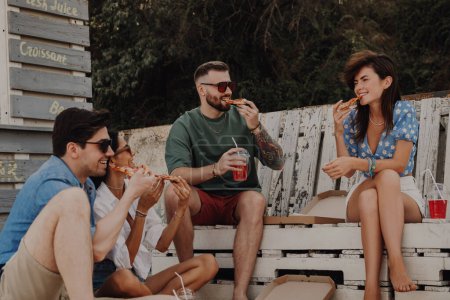 Téléchargez les photos : Groupe d'amis joyeux profitant de la nourriture et des boissons tout en se relaxant près du café de la plage ensemble - en image libre de droit
