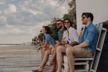 Téléchargez les photos : Groupe de jeunes amis joyeux profitant de la bière tout en passant du temps insouciant près de la maison de la plage - en image libre de droit