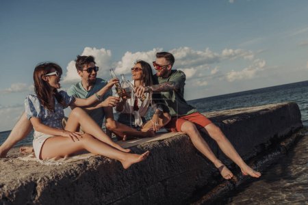 Photo for Group of young friends toasting with beer and smiling while spending time seaside together - Royalty Free Image