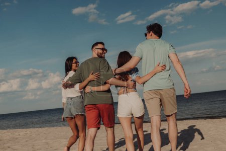 Téléchargez les photos : Vue arrière de jeunes gens heureux marchant vers la mer au bord de la plage - en image libre de droit