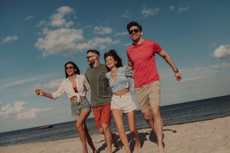 Foto de Grupo de jóvenes amigos felices que se unen y sonríen mientras corren por la playa juntos - Imagen libre de derechos