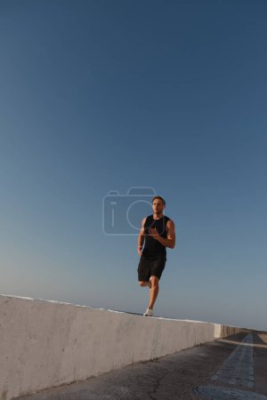 Téléchargez les photos : Jeune athlète masculin confiant en vêtements de sport profitant du jogging matinal en plein air - en image libre de droit
