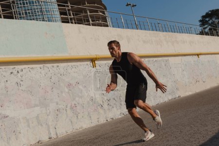 Téléchargez les photos : Pleine longueur de jeune athlète masculin confiant dans les vêtements de sport courir à l'extérieur - en image libre de droit