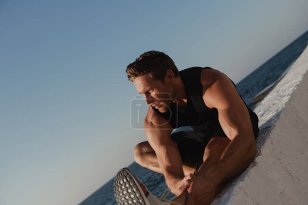 Photo for Handsome young male athlete in sports clothing warming up before jogging seaside - Royalty Free Image