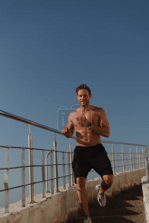 Foto de Feliz atleta masculino corriendo por las escaleras al aire libre con un cielo azul en el fondo - Imagen libre de derechos
