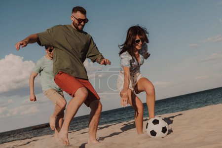 Foto de Tres jóvenes alegres pasan el día de verano juntos mientras juegan fútbol de playa - Imagen libre de derechos