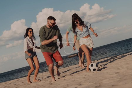Foto de Grupo de jóvenes alegres que pasan tiempo sin preocupaciones mientras juegan al fútbol en la playa - Imagen libre de derechos