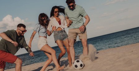 Foto de Grupo de jóvenes felices pasando tiempo sin preocupaciones mientras juegan al fútbol en la playa - Imagen libre de derechos