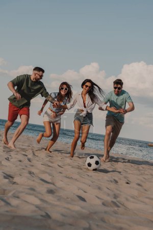 Téléchargez les photos : Groupe de jeunes heureux passant du temps insouciant ensemble tout en jouant au football de plage - en image libre de droit