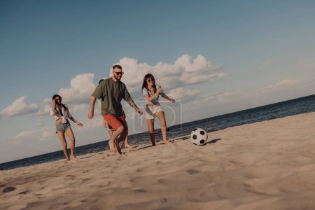 Foto de Grupo de jóvenes alegres pasando tiempo divertido juntos mientras juegan al fútbol en la playa - Imagen libre de derechos