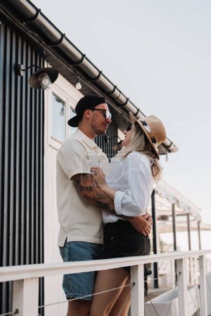 Téléchargez les photos : Jeune couple romantique embrassant et souriant tout en passant la journée d'été sur la terrasse de la maison ensemble - en image libre de droit