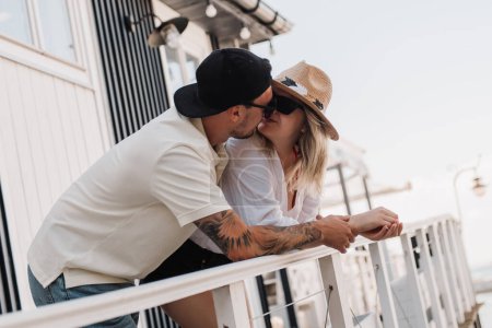 Téléchargez les photos : Jeune couple romantique embrasser tout en passant la journée d'été sur la terrasse vue mer ensemble - en image libre de droit