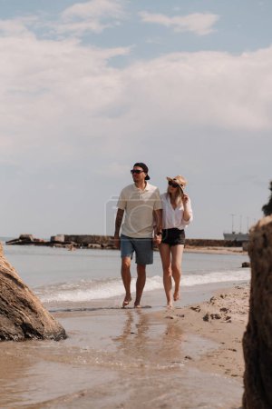 Téléchargez les photos : Pleine longueur de jeune couple romantique tenant la main tout en marchant sur la plage ensemble - en image libre de droit