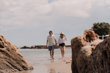 Téléchargez les photos : Beau jeune couple tenant la main tout en marchant sur la plage ensemble - en image libre de droit