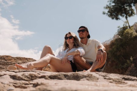 Photo for Beautiful young loving couple enjoying the scenery while sitting on the rocky mountain together - Royalty Free Image