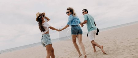 Photo for Three joyful friends spending fun time while running by the beach to the sea together - Royalty Free Image