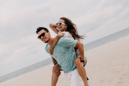Foto de Guapo joven a cuestas su novia feliz mientras se divierten en la playa juntos - Imagen libre de derechos