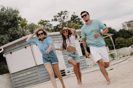 Foto de Tres jóvenes amigos felices pasando tiempo sin preocupaciones mientras corren por la playa juntos - Imagen libre de derechos