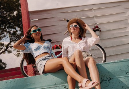 Téléchargez les photos : Deux jeunes femmes gaies regardant détendues tout en profitant de la journée d'été en plein air ensemble - en image libre de droit