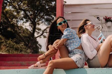 Téléchargez les photos : Deux jeunes femmes joyeuses regardant détendues tout en appréciant la journée d'été en plein air ensemble - en image libre de droit